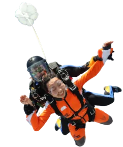 Smiling passenger in an orange jumpsuit and tandem instructor in freefall with the drogue chute above them